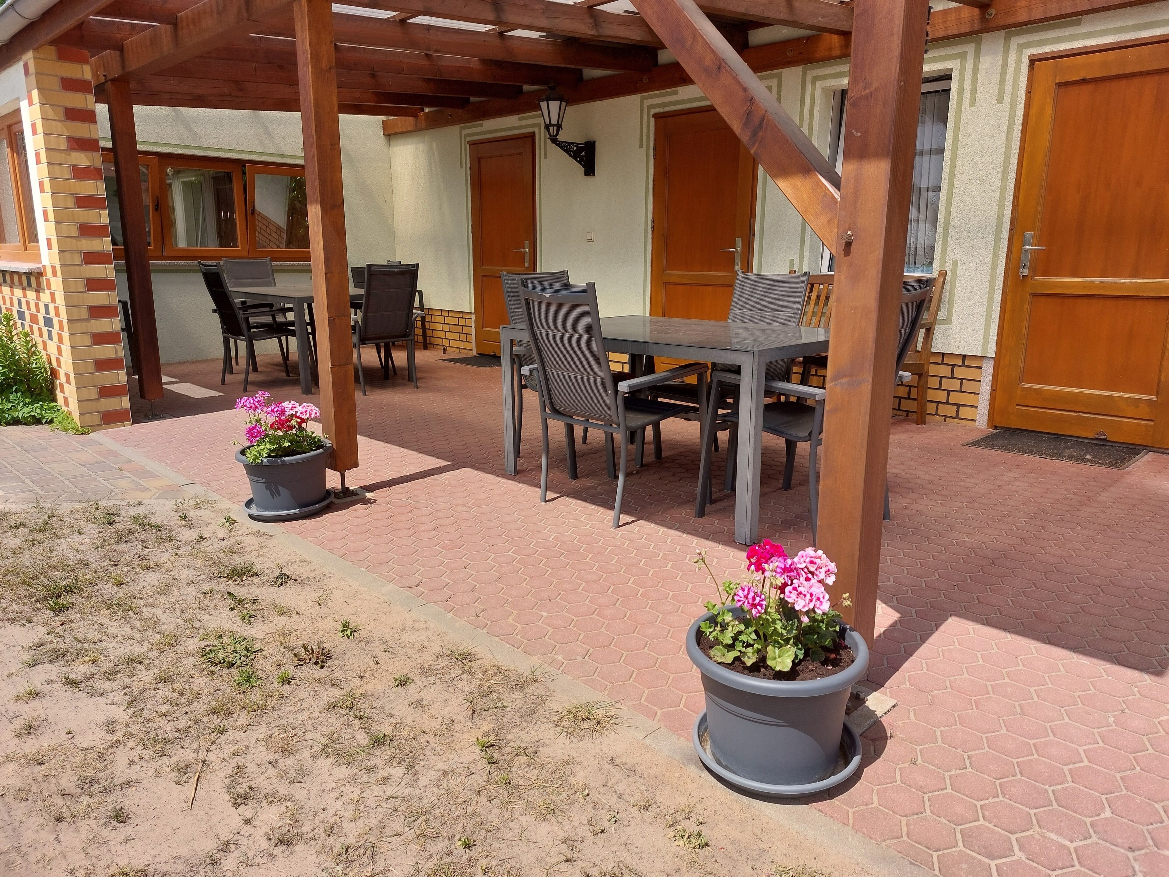 A covered patio area with a table and chairs, potted plants, and a wooden door.. Family-friendly vacation apartment in the Dahme-Heideseen Nature Park |Dogs welcome