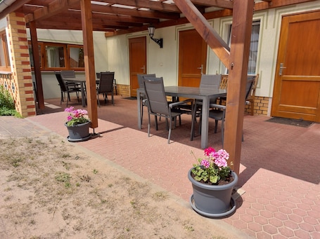 A covered patio area with a table and chairs, potted plants, and a wooden door.. Family-friendly vacation apartment in the Dahme-Heideseen Nature Park |Dogs welcome