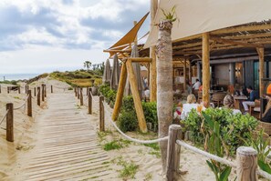 A wooden boardwalk leading to a beachside restaurant with outdoor seating and a covered area. - Nordic Bliss Marbella Townhouse (Marbella)