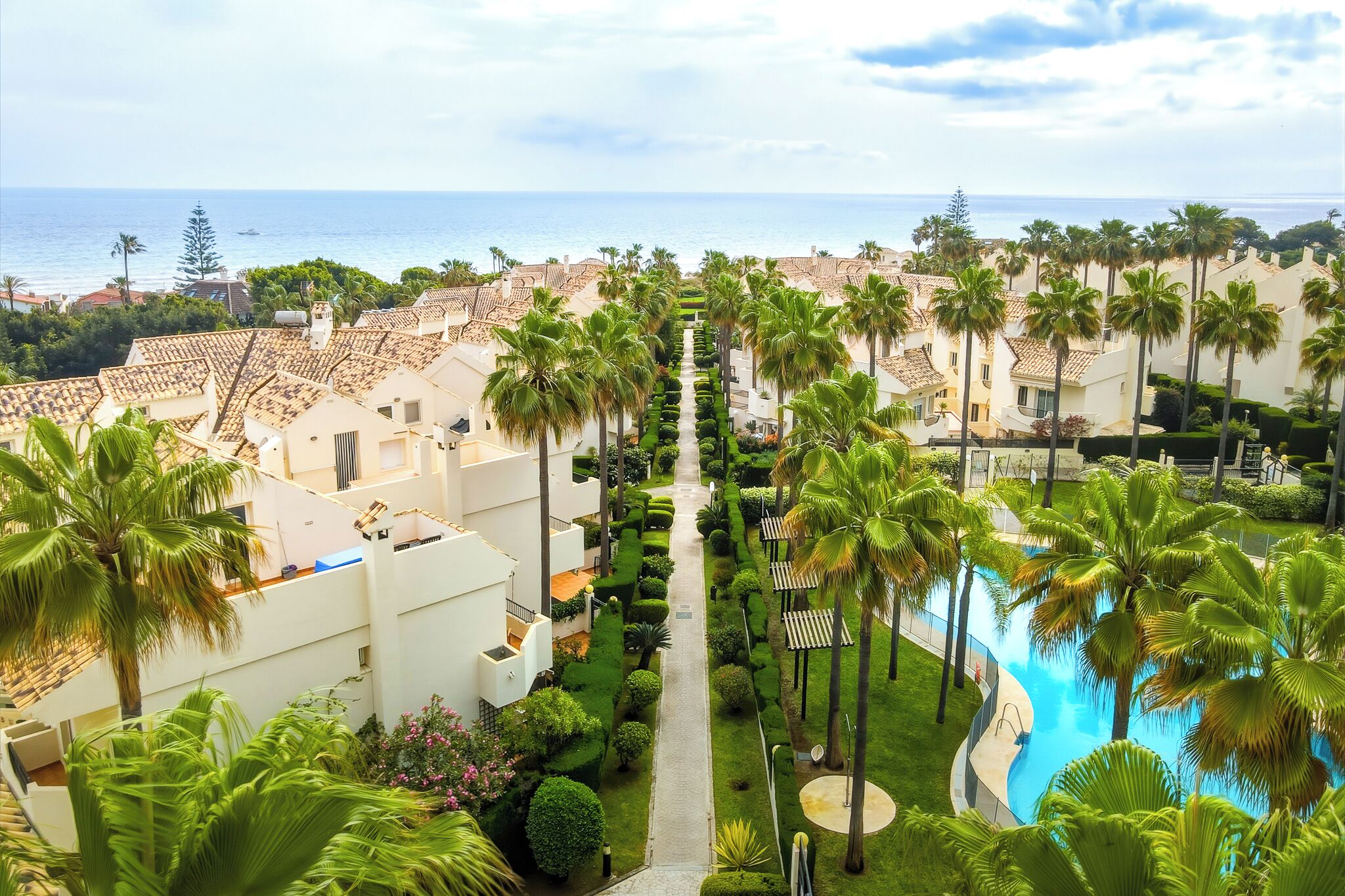 A resort with a pool, palm trees, and a view of the sea.