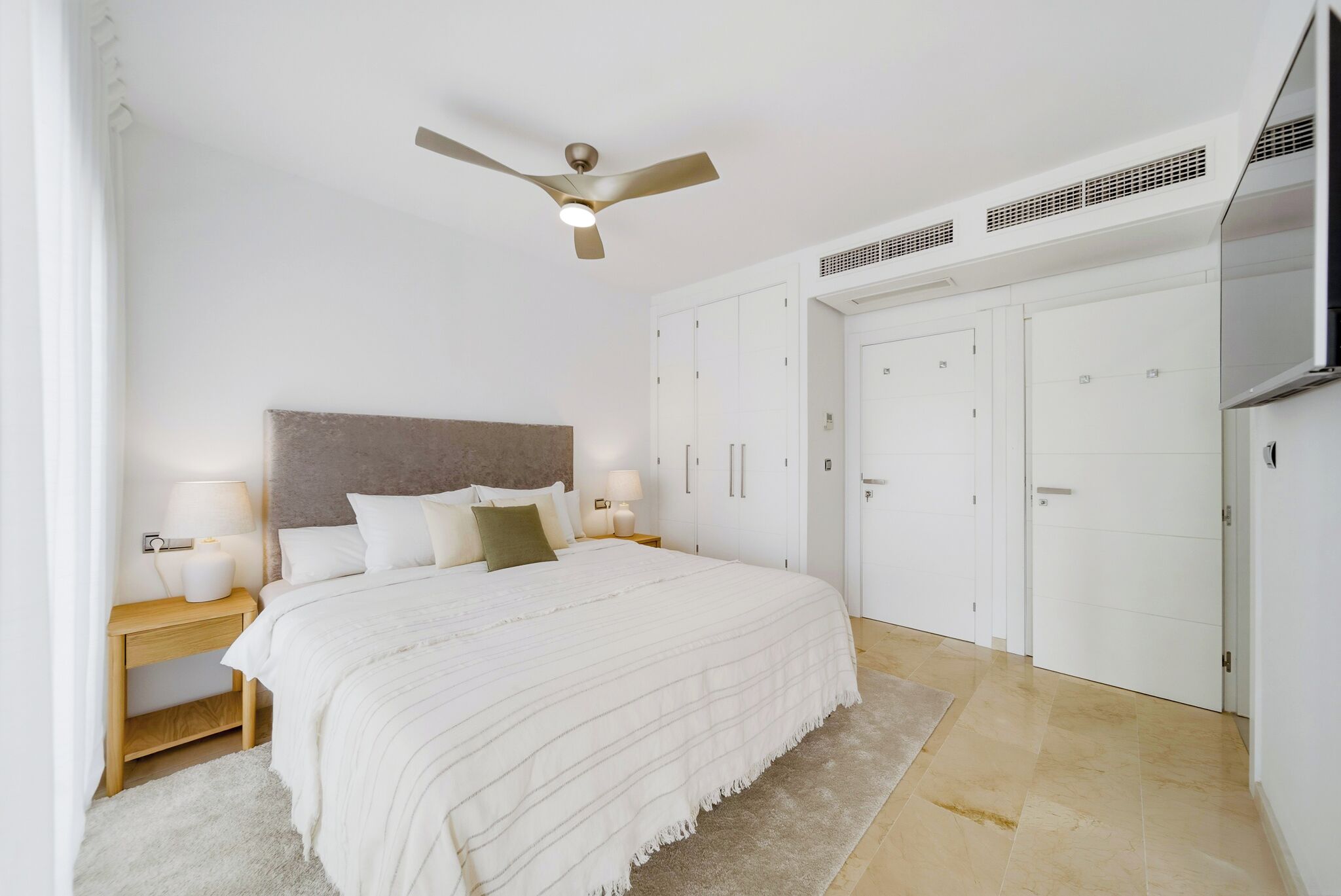 Une chambre à coucher comprenant un lit, des tables de chevet, un ventilateur de plafond et une armoire.