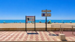 Una playa con un paseo pavimentado, un cartel con indicaciones y sombrillas de playa.
