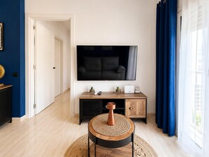 A modern living room with a flat-screen TV, a wooden coffee table, and a blue curtain. - Apartment for 3, a Short Walk From the Beaches (Roquetas de Mar)