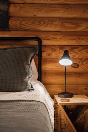 A wooden bed with a textured pillow and a bedside lamp on a wooden nightstand. - Romantic Cabin * Sauna * Hot tub * King Suite (Sevierville)