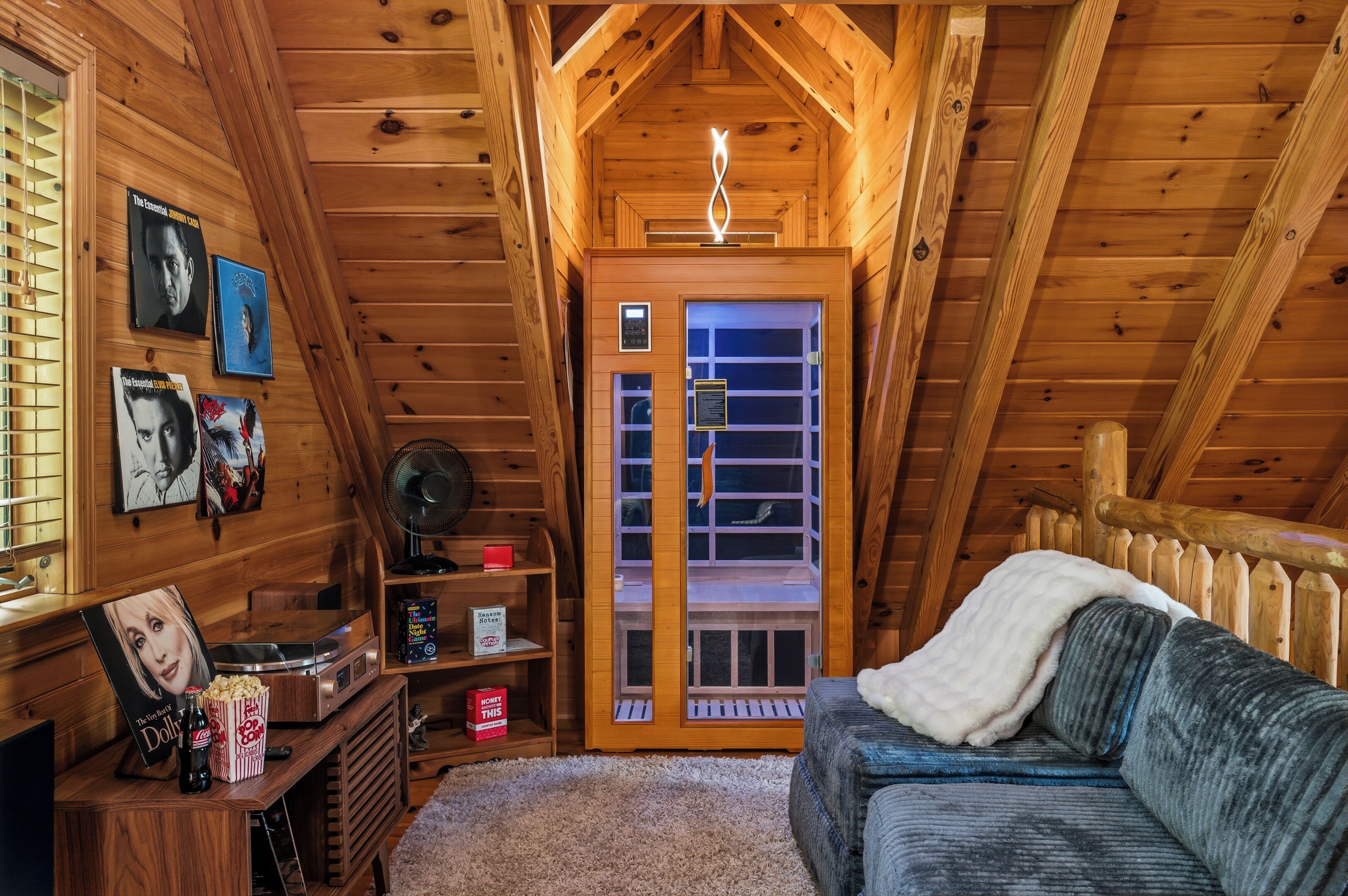 L’intérieur d’un chalet accueillant, avec un plafond en bois, une télévision, un ventilateur, un canapé et une porte donnant sur un balcon.