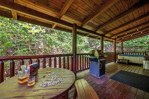 A wooden deck with a barbecue grill, a table with a puzzle, and a glass of whiskey. - Romantic Cabin * Sauna * Hot tub * King Suite (Sevierville)