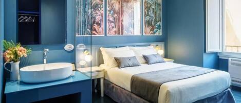 Quarto moderno com cama grande, mesa de cabeceira, lavatório embutido e espelho.