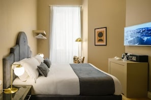 Una habitación de hotel con cama, escritorio con lámpara, televisor y ventana con cortinas.