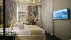 A modern hotel room with a large bed, a TV mounted on the wall, and a cityscape view. - Birkin Porto 1870 (Cagliari)