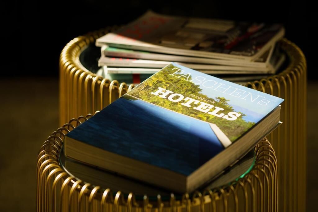 Un libro con el título 'TASCHEN'S HOTELS' sobre una mesa de mimbre junto a algunas revistas.