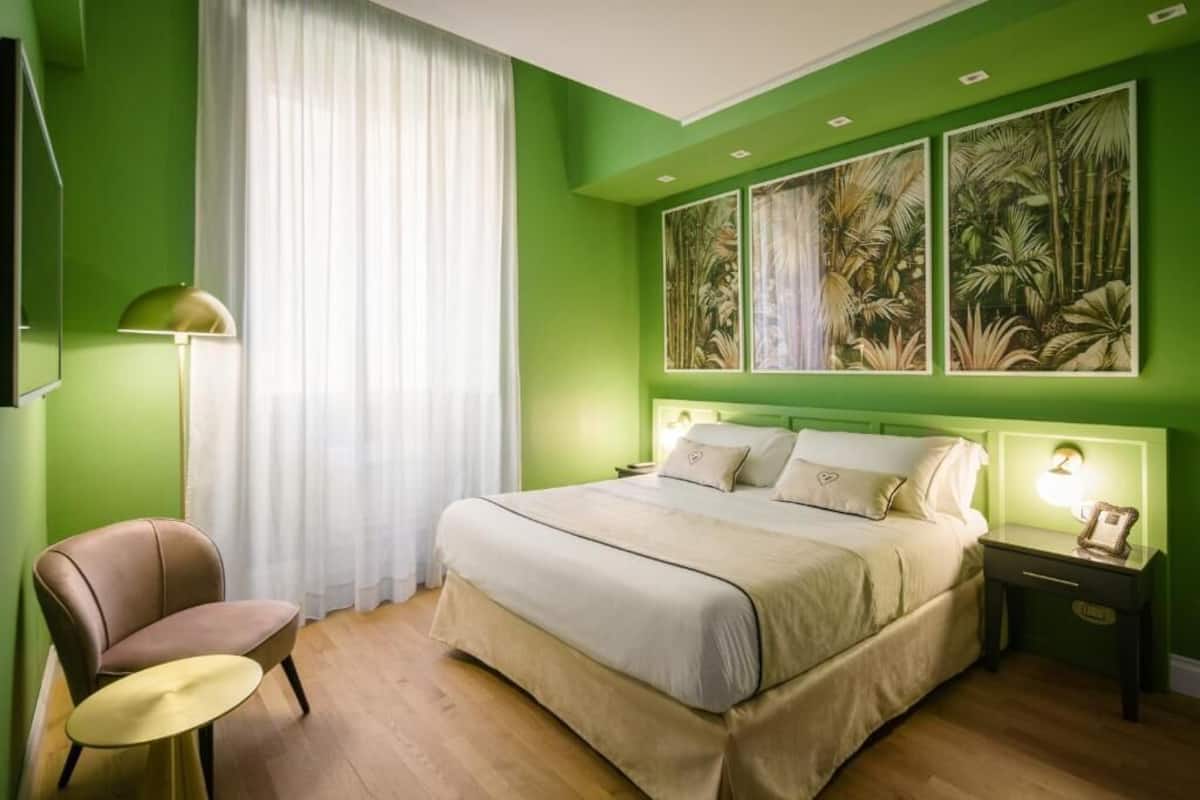 A bedroom with a bed, a chair, a bedside table, and a wall with three framed pictures.