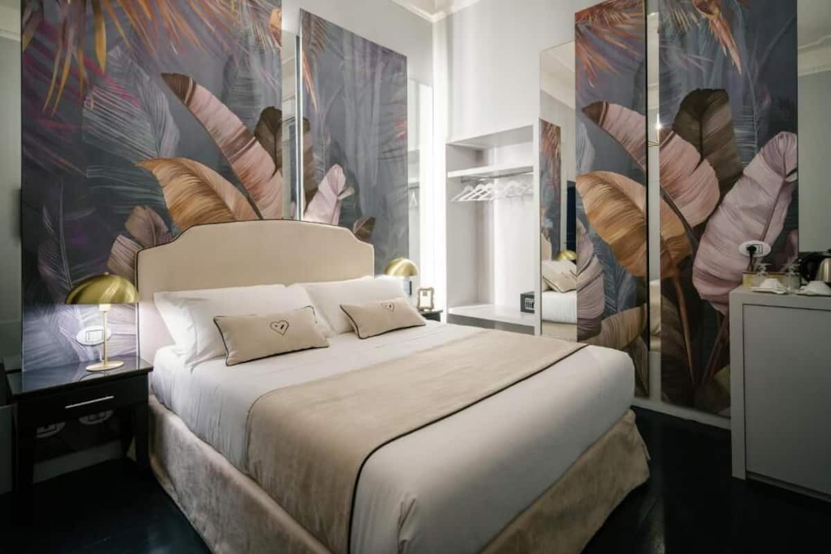 A modern hotel room with a large bed, a nightstand, a desk, and a wardrobe.