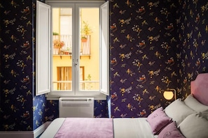 A bedroom with a bed, a window, and a wall with a floral pattern. - Birkin Porto 1870 (Cagliari)