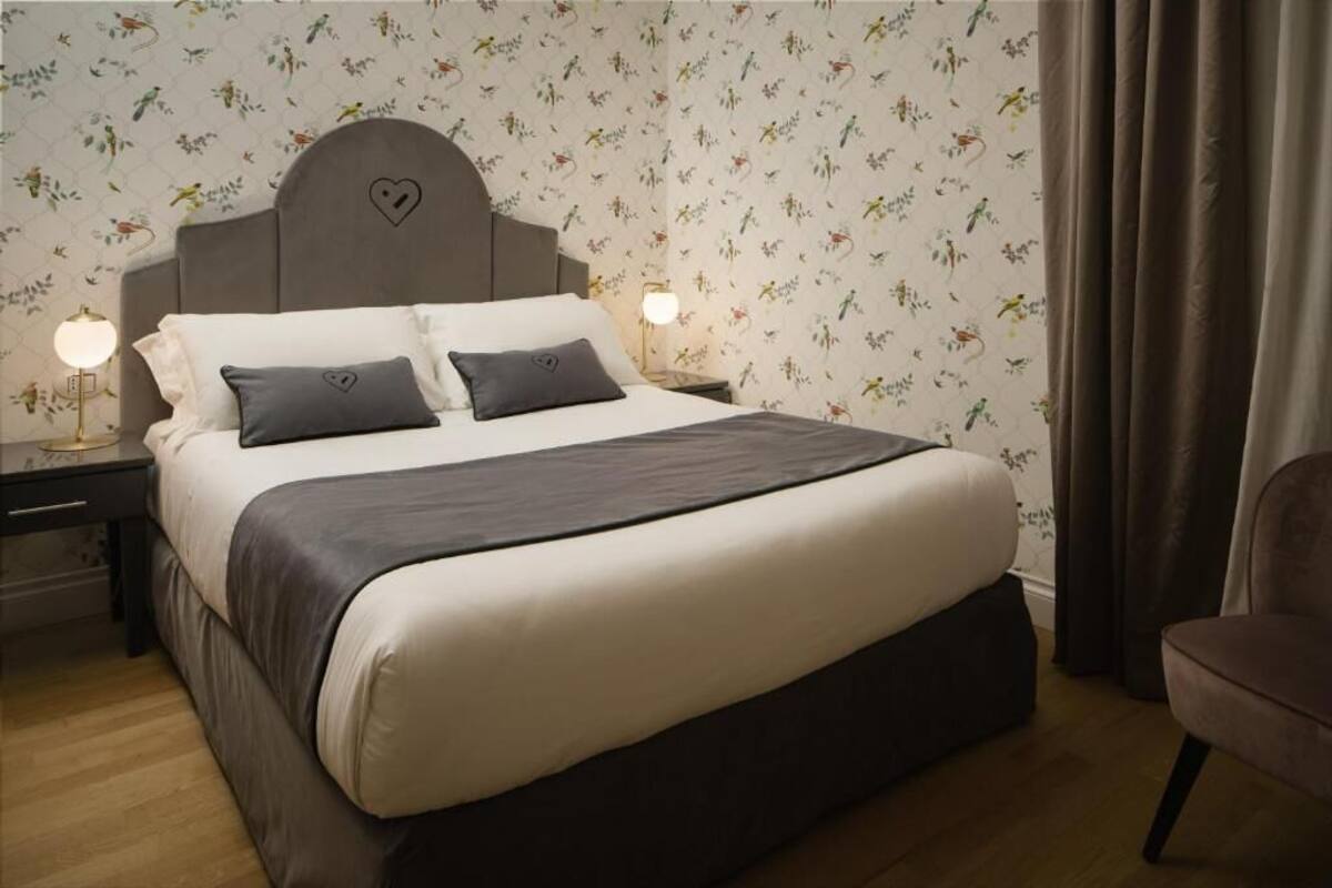 A bedroom with a bed, nightstands, a chair, and floral wallpaper.