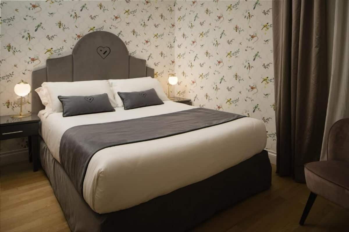 Une chambre à coucher avec un lit, des tables de chevet, une chaise et un papier peint à motifs floraux.