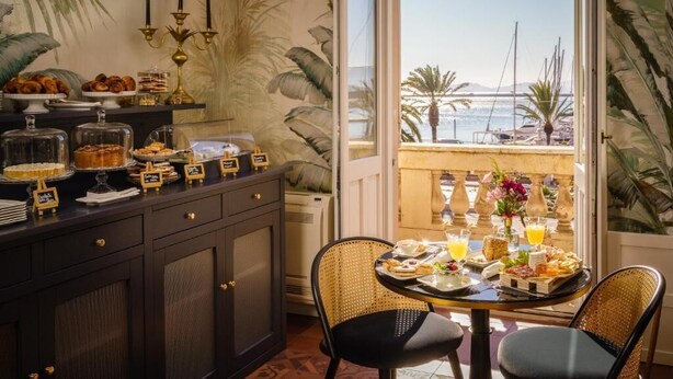 A breakfast setup with a buffet, a table with chairs, and a view of the sea through a balcony. - Birkin Porto 1870 (Cagliari)