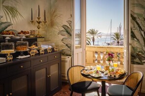 Een ontbijtarrangement met een buffet, een tafel met stoelen en uitzicht op zee vanaf een balkon.