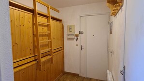 Een kamer met houten lambrisering, een witte deur, een plafondlamp en een klein plankje met spullen.