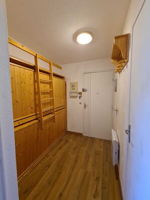 Ein Zimmer mit Holzwänden, einer weißen Tür, einer Deckenleuchte und einem kleinen Regal mit Gegenständen.