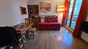 Een gezellige woonkamer met een houten eettafel, een rode bank, een kast met glazen deuren en een groot raam met gordijnen.