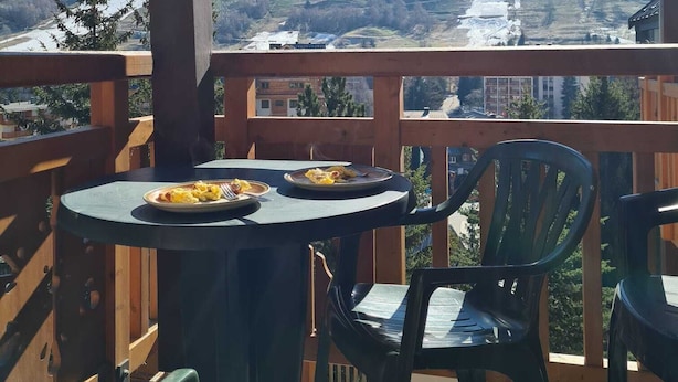 Een balkon met een tafel en stoelen, met uitzicht op een bergachtig landschap.