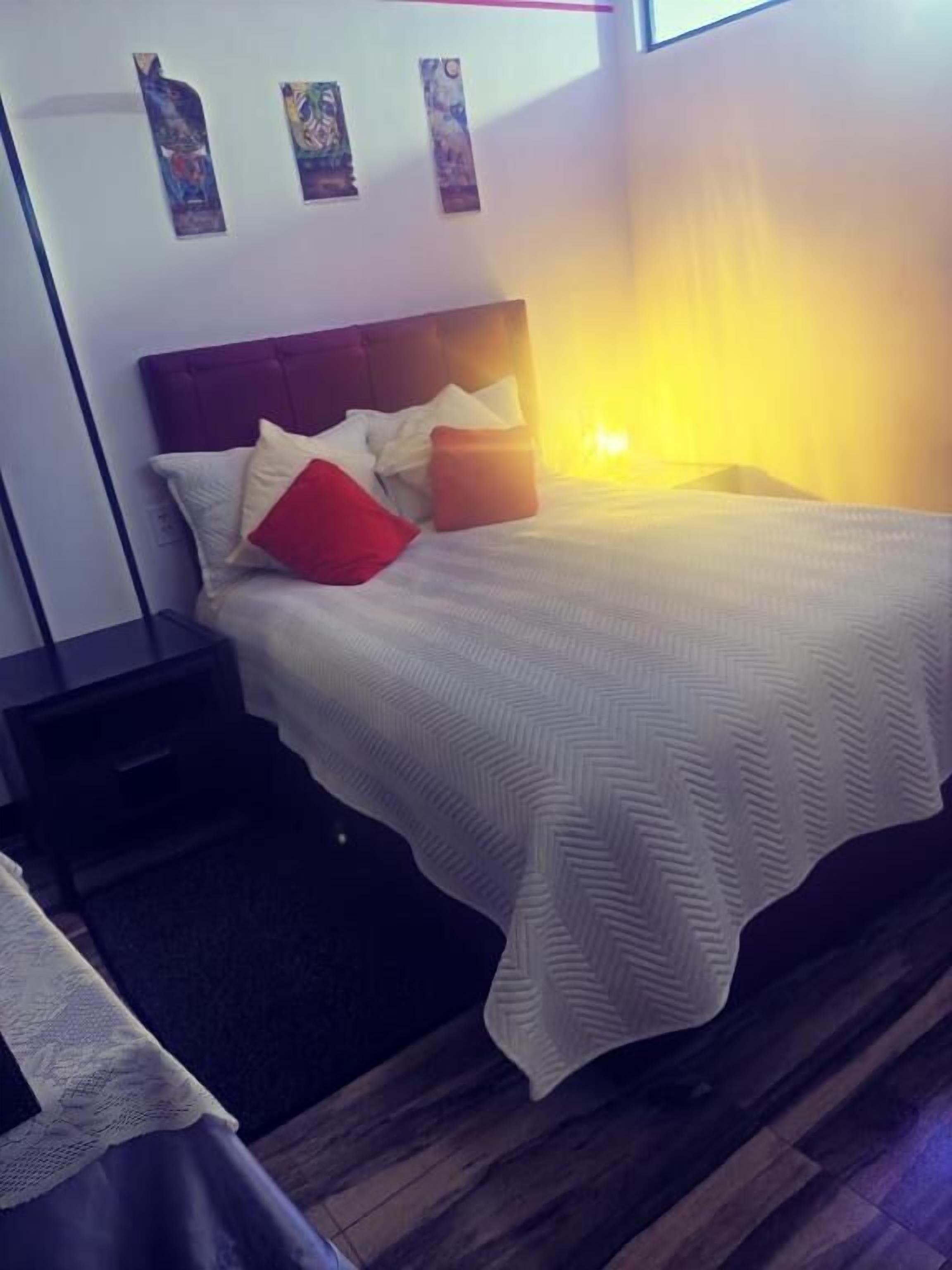 Ein ordentlich gemachertes Bett mit weißer Bettdecke und Kissen, ein Nachttisch aus Holz und eine Wand mit drei gerahmten Bildern.