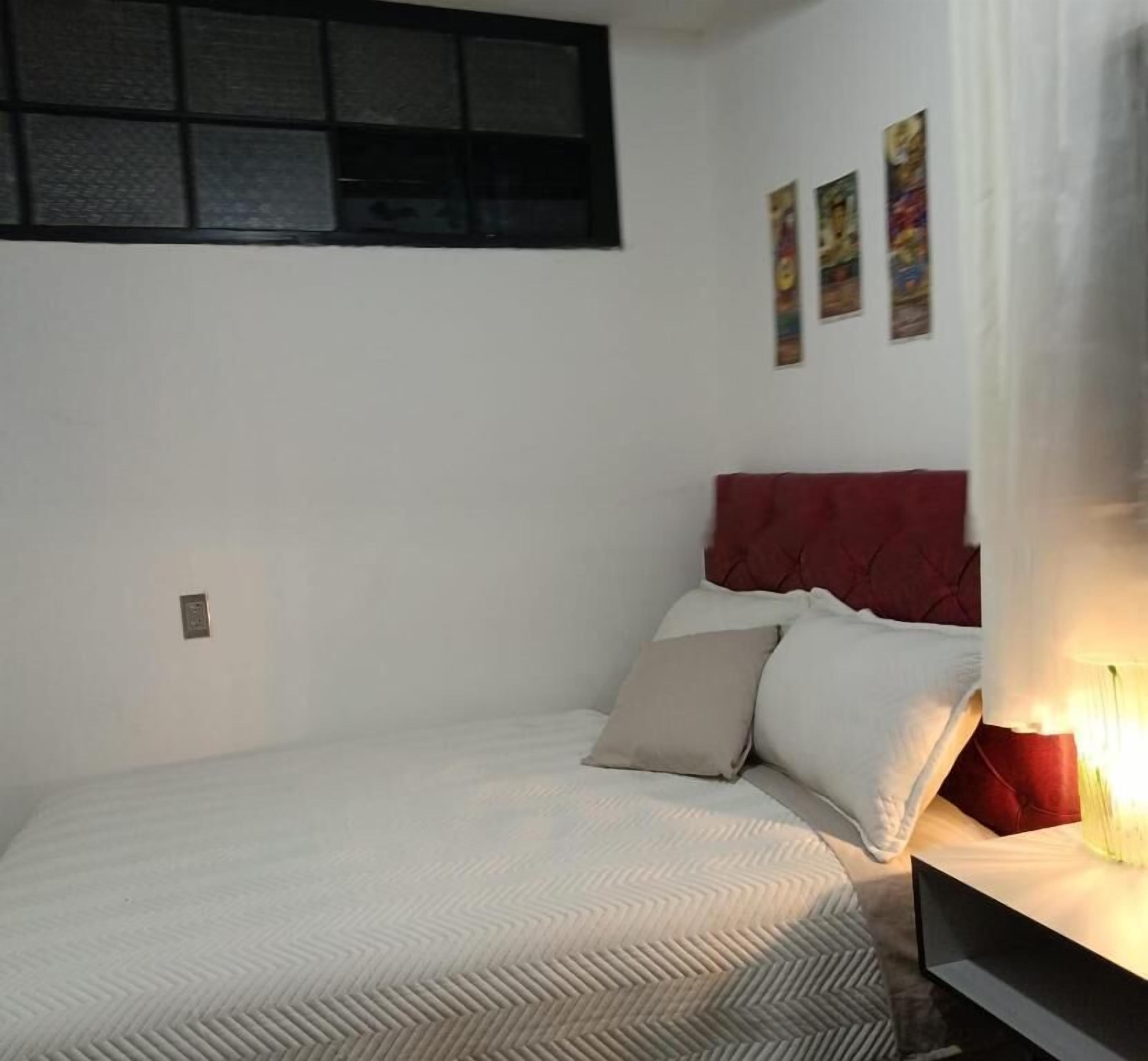 A bedroom with a bed, a red headboard, and a wall-mounted shelf.