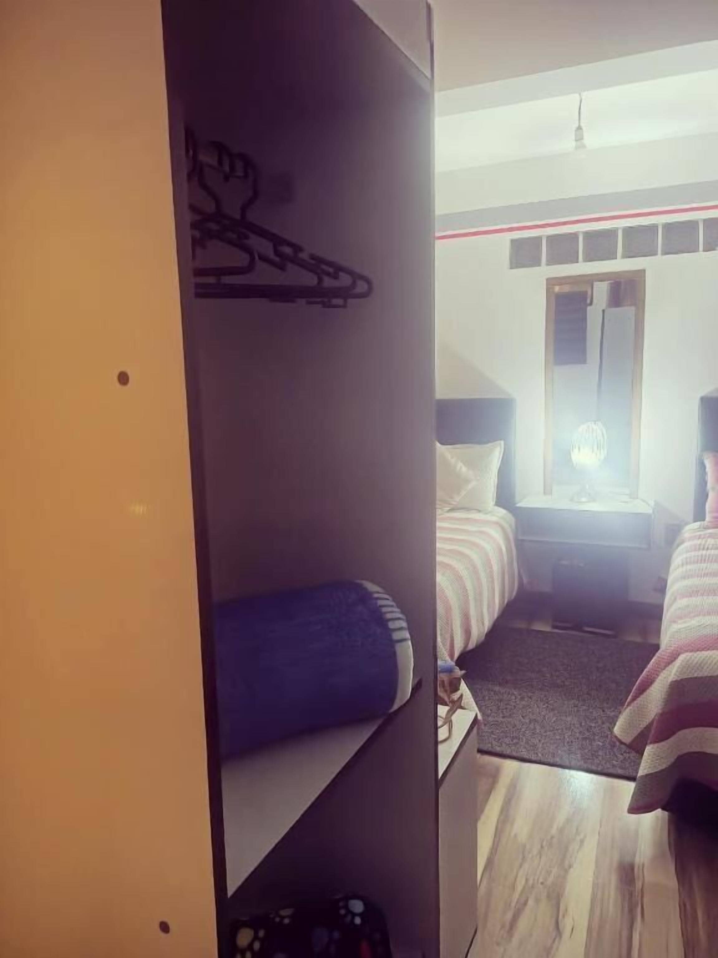 A bedroom with a bunk bed, a desk, a chair, and a hanging coat rack.