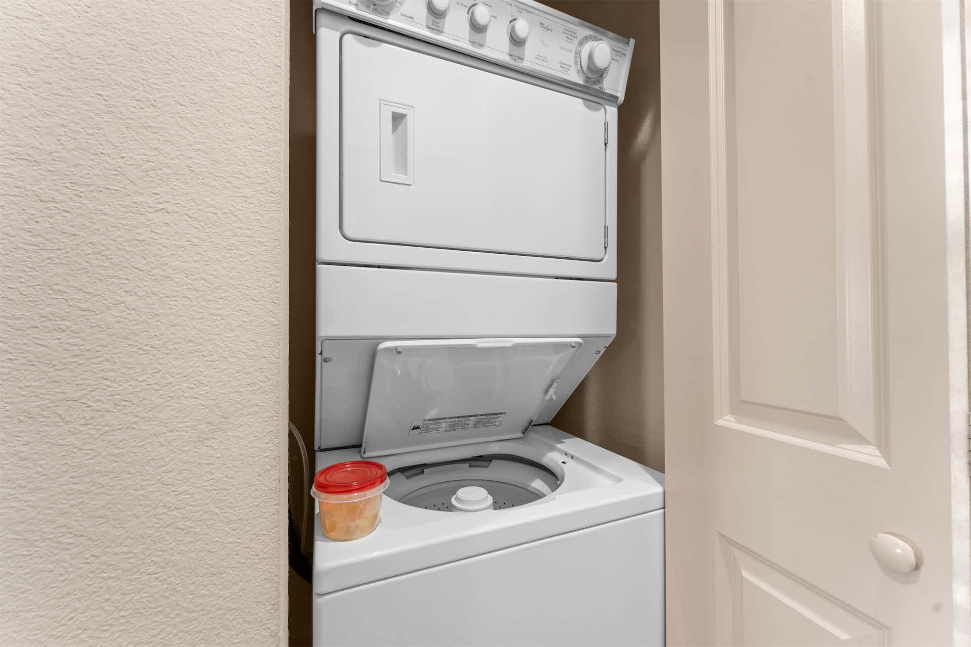 A compact washer and dryer unit in a small laundry room with a door to the right.