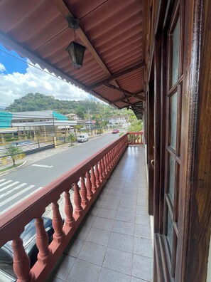 Ein Balkon mit roter Brüstung, Blick auf eine Straße mit Autos und ein Gebäude im Hintergrund.