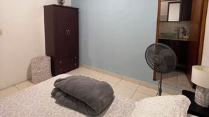 Et soveværelse med seng, natbord, kommode, ventilator og spejl.
