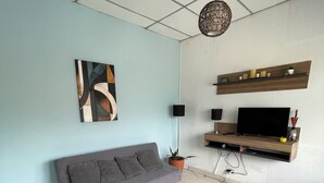 En stue med sofa, fjernsyn, en plante og en vægmonteret reol.