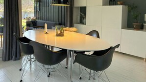 A modern dining area with a round table, black chairs, a pendant light, and a view of the outdoors. - Authentic timber house with forest near Ebeltoft (Ebeltoft)