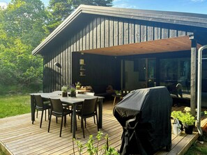 Une terrasse en bois avec une table et des chaises, un barbecue et des plantes en pot.