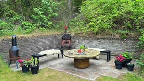 Une terrasse extérieure avec une table ronde, des chaises, un barbecue et des plantes en pot.