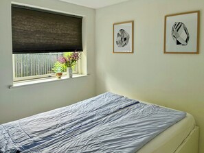 Une chambre à coucher avec un lit, une fenêtre avec un store et deux œuvres d’art encadrées accrochées au mur.