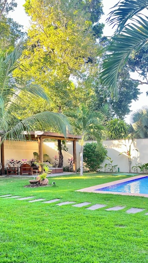 Um jardim bem cuidado com piscina, pérgola e diversas plantas.