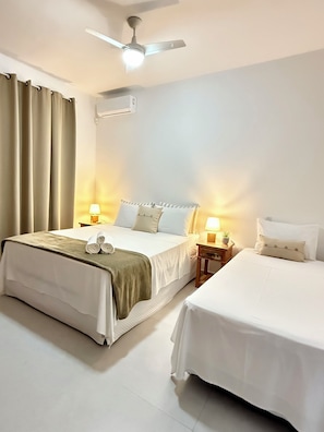A hotel room with a bed, bedside tables, a ceiling fan, and a window with curtains. - Arraial d'Ajuda House with Private Pool (Arraial d'Ajuda)