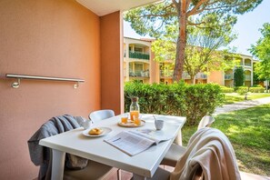 Una mesa con alimentos para el desayuno, una silla, una toalla y una ventana con vistas a un patio con edificios.