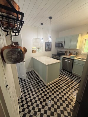 Una cocina con piso a cuadros, una isla central, lámparas colgantes y electrodom ésticos de acero inoxidable.
