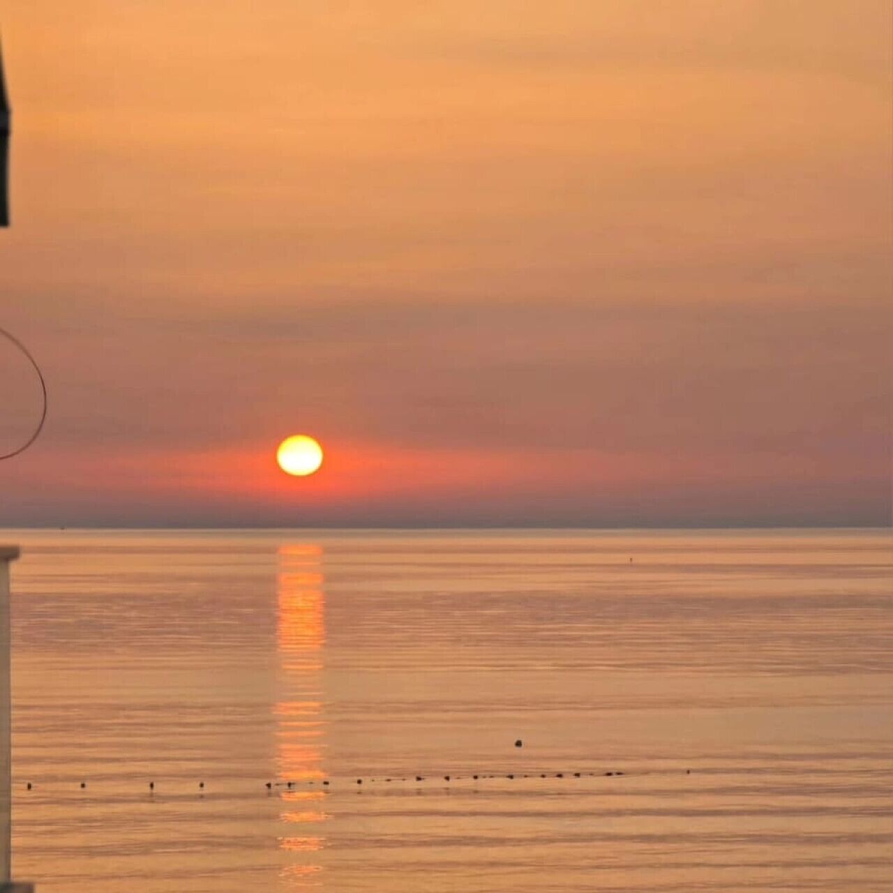 Een zonsondergang boven een kalme zee met een pier die zich in het water uitstrekt.