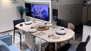 A modern dining area with a round table, chairs, and a television displaying a show. - Sea Dream Studio Qerret (Golem)