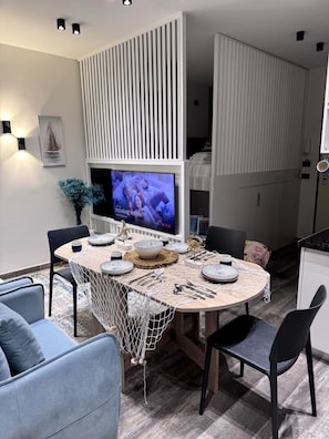 A modern dining area with a round table, chairs, and a television displaying a show. - Sea Dream Studio Qerret (Golem)