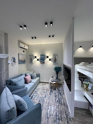 A modern living room with a grey sofa, a patterned rug, wall-mounted lights, and a fireplace. - Sea Dream Studio Qerret (Golem)