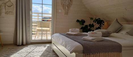A cozy bedroom with a bed, a large window, and a balcony.