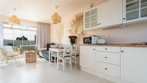 Een lichte keuken met witte kasten, een eethoek met een tafel en stoelen, en een groot raam met uitzicht.