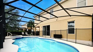 Ein Schwimmbad mit überdachtem Bereich, eine Terrasse mit Stühlen und ein Gebäude im Hintergrund.