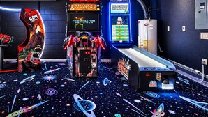 Ein Spielzimmer mit Arcade-Automaten, einer Neonreklame und einem bodenständigen Weltraumdesign.