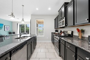A modern kitchen with dark cabinets, granite countertops, a built-in oven, and a window with blinds. - Spacious modern home w/ private arcade, pool and spa (Davenport)