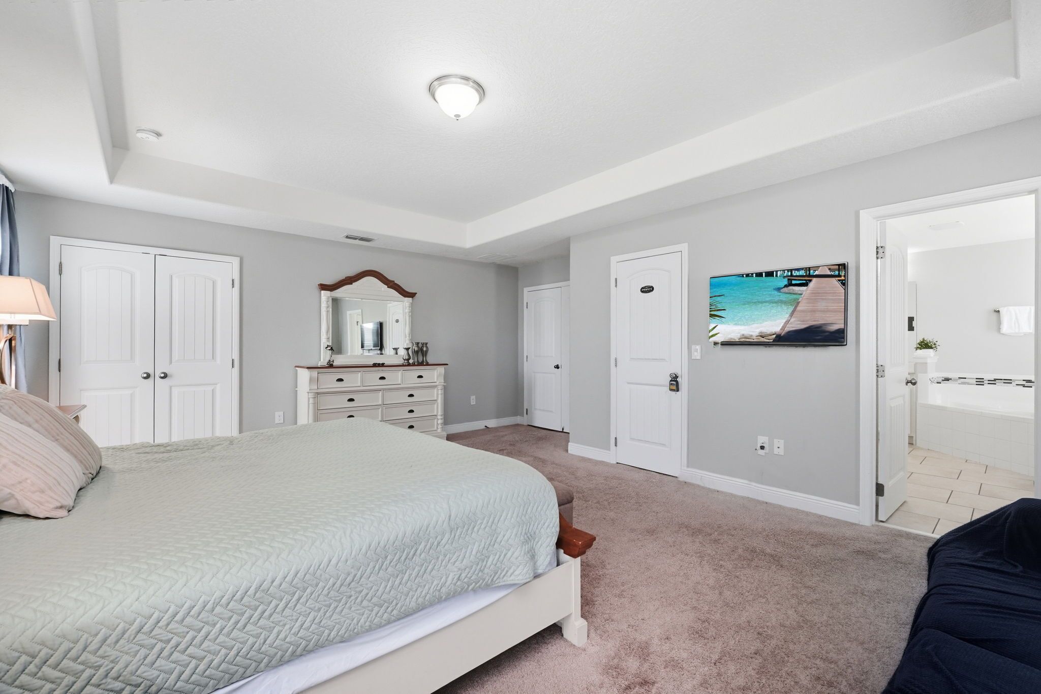 A bedroom with a bed, a dresser, a mirror, and a door leading to a bathroom.